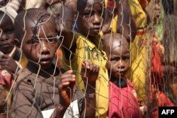 FILE - Burundian children, who fled their country, stand behind a fence at Nyarugusu camp, Tanzania, June 11, 2015.