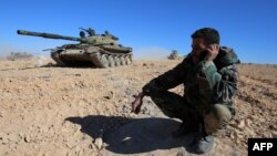 FILE - A member of the Syrian pro-government forces speaks on a mobile phone as troops gather on a hilltop overlooking the town of Mahin, which is under control of the Islamic State group, in Homs province, Nov. 14, 2015.