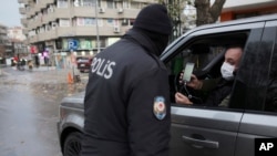 A man wearing a mask to help protect against the spread of coronavirus, shows a document as a police officer checks IDs during a two-day weekend curfew, in Ankara, Turkey, Dec. 13, 2020. 