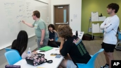 George Mason undergraduate math major David Wigginton writes an equation on a whiteboard as students Ethan Hill, right, and Diego Fonseca, center, take part in a summer math boot camp on Thursday, Aug. 1, 2023 at George Mason University in Fairfax. Va. (AP Photo/Kevin Wolf)