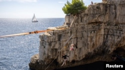 Para peserta ambil bagian dalam festival bergelantungan di atas laut dengan tali baja di kota Pula, Kroasia. 