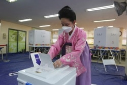 FILE - A woman wearing a face mask to help protect against the spread of the new coronavirus casts a vote for the parliamentary elections at a polling station in Seoul, South Korea, Wednesday, April 15, 2020.