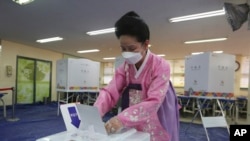 A woman wearing a face mask to help protect against the spread of the new coronavirus casts a vote for the parliamentary elections at a polling station in Seoul, South Korea, April 15, 2020. 