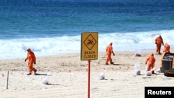 Workers in protective clothing clean up unknown debris washed up on Coogee Beach, Sydney, Oct. 17, 2024. (AAP/Dan Himbrechts via Reuters)