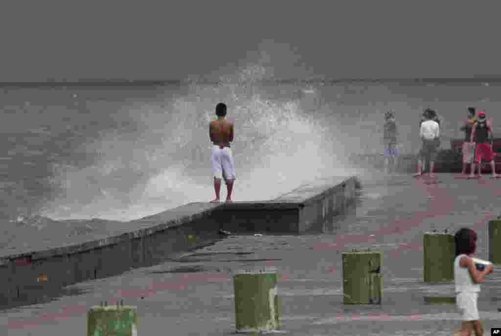 A boy stands as waves hit a wall at a park in Navotas, north of Manila, Philippines.