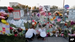 FILE - People light candles at a makeshift memorial outside Marjory Stoneman Douglas High School, where 17 students and faculty were killed in a mass shooting days earlier in Parkland, Fla.