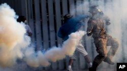 Anti-government protesters throw back tear gas canisters to riot policemen during a clash at a sport stadium in Bangkok, Thailand, Dec. 26, 2013. 