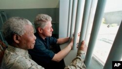 FILE - Nelson Mandela, left, and former US president Bill Clinton look to the outside from Mandela's Robben Island prison cell in Cape Town, South Africa, March 27, 1998.