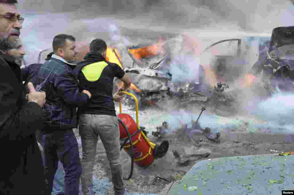 Bombeiros deslocam um extintor enquanto um membro do Hezbollah transporta um walkie-talkie no local da explosão em Haret Hreik, Beirute, Jan. 21, 2014.