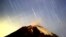 FILE - The Geminid meteor shower lights up the sky over the Mexican volcano Popocatepetl near the village of San Nicolas de los Ranchos in Puebla state, early on Dec. 14, 2004. The show for 2018 is peaking overnight on Dec. 13 and 14.