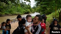 Seorang migran menggendong anaknya setelah berhasil melalui Celah Darien dan tiba di pusat penerimaan migran di desa Lajas Blancas, Panama, pada 26 September 2024. (Foto: Reuters/Enea Lebrun)