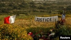 FILE - A banner calling for justice is seen next to a photo of assassinated anti-corruption journalist Daphne Caruana Galizia at the bomb site, in Bidnija, Malta, April 15, 2018.