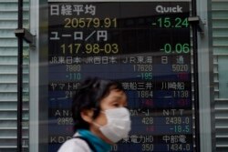 A masked woman walks past an electronic stock board showing Japan's Nikkei 225 index at a securities firm in Tokyo, May 21, 2020.