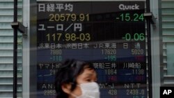 A masked woman walks past an electronic stock board showing Japan's Nikkei 225 index at a securities firm in Tokyo Thursday, May 21, 2020. Asian stock markets are mixed after Wall Street rose amid Chinese trade tension with Washington and Australia…