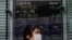 A masked woman walks past an electronic stock board showing Japan's Nikkei 225 index at a securities firm in Tokyo on May 21, 2020.