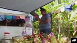 In this image from video, a woman prays in front of a portrait of her lost child with measles in Apia, Samoa. Samoa closed all its schools, Nov. 18, 2019, banned children from public gatherings and mandated that everybody get vaccinated.