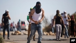 Palestinian demonstrators throw stones toward Israeli security forces during clashes after the funeral of Palestinian Saed Dawabsheh who died after an arson attack on his family's home, in the West Bank village of Duma near Nablus, Aug. 8, 2015. 