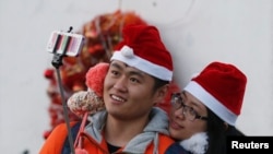 FILE - A couple wearing Santa hats take a "selfie" at a Catholic church in Beijing, December 24, 2014.