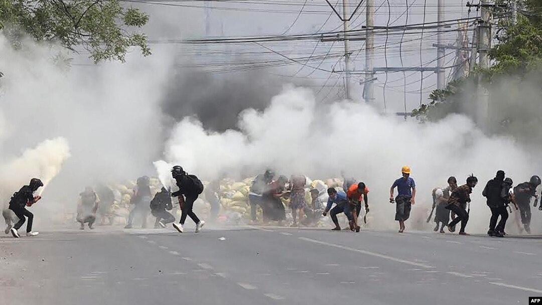Protesters run from tear gas fired by security forces, as some demonstrators also let off fire extinguishers, next to a barricade set up during the demonstration against the military coup in Mandalay, March 15, 2021.