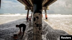 Anak-anak bermain di bawah dermaga pantai Jacksonville menjelang badai Dorian di Jacksonville, Florida, 3 September 2019. 