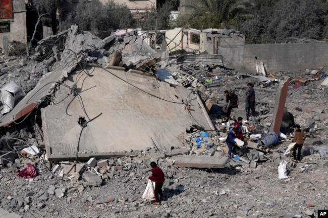 Warga Palestina menyelamatkan barang-barang dari reruntuhan bangunan keluarga Hamad yang hancur akibat serangan Israel di Deir al Balah, Jalur Gaza, Jumat, 29 Desember 2023. (Foto: AP/Adel Hana)