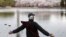 A man removes his mask to stretch and take a deep breath across from cherry blossoms at the Yuyuantan Park in Beijing on Thursday, March 26, 2020. 