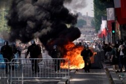 Members of the Gendarmerie stand in front of fences and a fire as protesters linked to the Yellow Vests movement (unseen) take part in a demonstration on the side of the annual Bastille Day ceremony, July 14, 2019, on the Champs-Elysees in Paris.