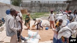 Les gens se rassemblent alors qu'un homme collecte des grains de blé lors d'une distribution de nourriture organisée par le gouvernement d'Amhara près du village de Baker, à 50 km au sud-est de Humera, dans la région du Tigré en Éthiopie, le 11 juillet 2021.