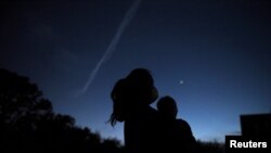 A woman holds her son while they view Jupiter and Saturn during a planetary conjunction, as they appear close together in a rare celestial event in Houston, Texas, Dec. 21, 2020.