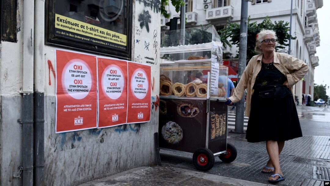 Seorang nenek penjual roti di sebelah poster bertuliskan "Tidak untuk proposal Uni Eropa, IMF dan ECB" di kota Thessaloniki, Yunani (1/7). (AP/Giannis Papanikos)