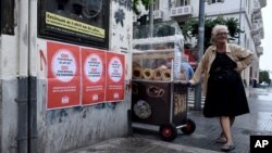 Seorang nenek penjual roti di sebelah poster bertuliskan "Tidak untuk proposal Uni Eropa, IMF dan ECB" di kota Thessaloniki, Yunani (1/7). (AP/Giannis Papanikos)