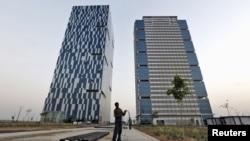 A worker folds the cable of a welding machine in front of two office buildings at the Gujarat International Finance Tec-City (GIFT) at Gandhinagar, in the western Indian state of Gujarat, April 10, 2015. 