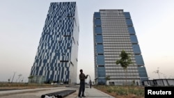 A worker folds the cable of a welding machine in front of two office buildings at the Gujarat International Finance Tec-City (GIFT) at Gandhinagar, in the western Indian state of Gujarat, April 10, 2015. 