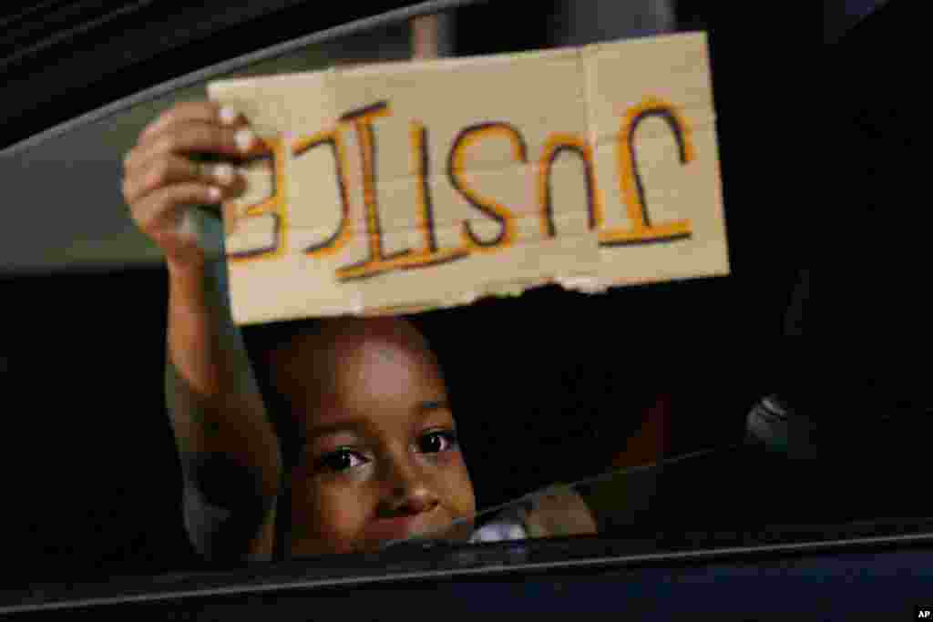 A young boy holds a &quot;Justice&quot; sign as he peers outside the window of a car passing protesters marching through downtown for a third night of unrest Sunday May 31, 2020, in Richmond, Va.