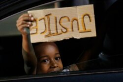 A young boy holds a 'Justice' sign as he peers outside the window of a car passing protesters marching through downtown for a third night of unrest May 31, 2020, in Richmond, Va.