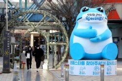A couple wearing face masks as a precaution against the coronavirus passes by a statue with a face mask at a shopping street in Goyang, South Korea, Nov. 28, 2020.
