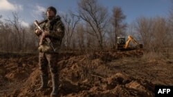 Arhiva - Ukrajinski vojnik na straži osmatra nebo kako bi uočio ruske dronove , dok bager kopa sistem rovova iza njega, u oblasti Zaporožja, tokom ruske invazije na Ukrajinu, 30. januara 2024.