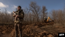 FILE - A Ukrainian serviceman stands guard checking for Russian drones in the sky as a soldier in a tractor digs a trench system in the Zaporizhzhia region, on January 30, 2024, amid the Russian invasion of Ukraine.