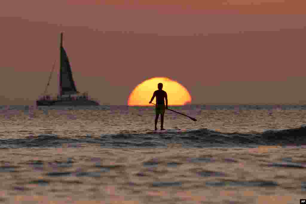 Seorang pria mendayung papan luncurnya sambil menikmati matahari penghujung tahun 2013 terbenam, di pantai Waikiki Lautan Pasifik, Honolulu, Hawaii.