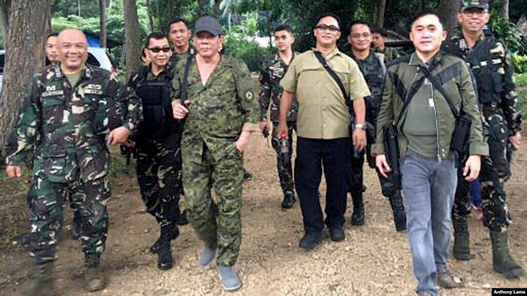 President Rodrigo Duterte, center left, wearing a cap and an assault rifle slung on his shoulder, walks with other military officers and security men inside the camp of the 2nd Mechanized Infantry Brigade, Light Armored Division, July 7, 2017, in the outskirts of Iligan city in southern Philippines. 