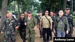 Presiden Rodrigo Duterte, kiri tengah, mengenakan topi dan membawa senapan, berjalan bersama anggota tentara.