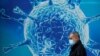 Great Britain, A man wearing a protective face mask walks past an illustration of a virus outside a regional science centre