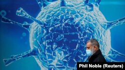 Great Britain, A man wearing a protective face mask walks past an illustration of a virus outside a regional science centre