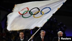 ເຈົ້າຄອງ ນະຄອນ Rio de Janeiro ທ່ານ Eduardo Paes (ຊ້າຍ) ໂບກທຸງໂອລິມປິກ ພ້ອມດ້ວຍ ປະທານອົງການ IOC ທ່ານ Jacque Rogge (ກາງ) ແລະ ເຈົ້າຄອງນະຄອນ London ທ່ານ Boris Johnson (ຂວາ) ໃນລະຫວ່າງພິທີປິດ ງານມະຫາກຳ ການແຂ່ງຂັນ ໂອລິມປິກ ປີ 2012 ຢູ່ທີ່ສະໜາມກິລາໂອລິມປິກ, ເມື່ອວັນທີ 12 ສິງຫາ 2012.