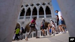 Tourists walks on a bridge in front of Palazzo Ducale, in Venice, Italy, Thursday, June 17, 2021. After a 15-month pause in mass international travel, Venetians are contemplating how to welcome visitors back to the picture-postcard canals and…