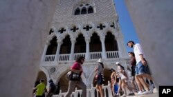 FILE - Tourists walk on a bridge in front of Palazzo Ducale, in Venice, Italy, June 17, 2021. 