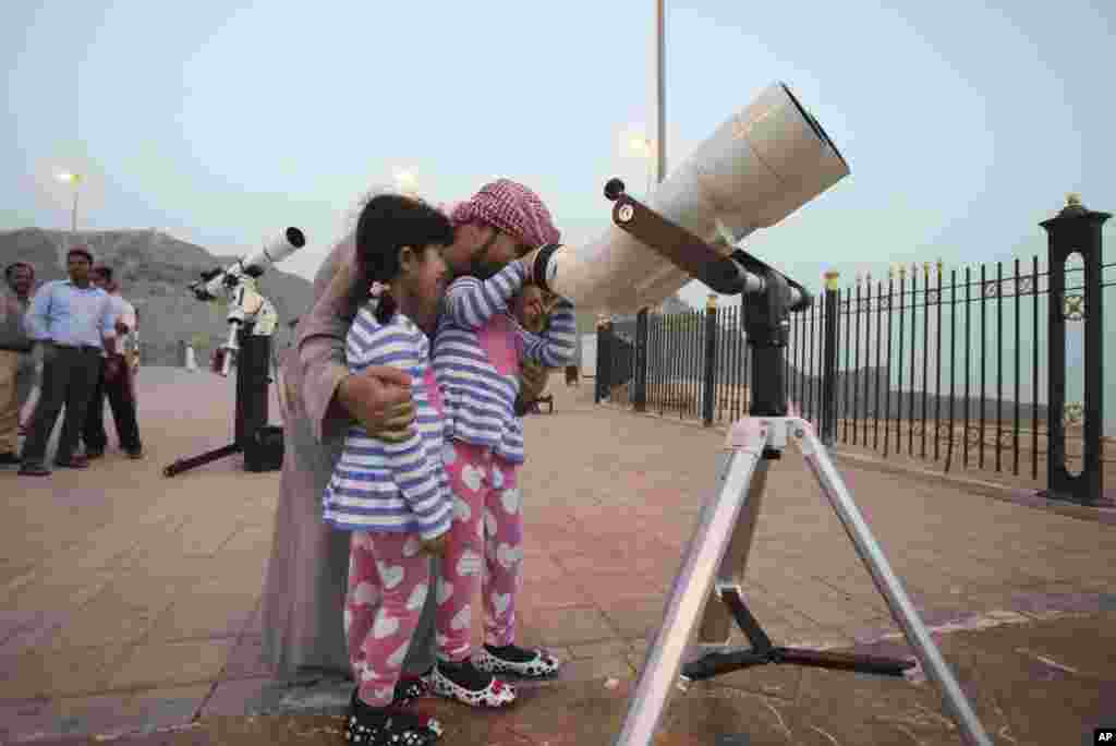 Seorang ayah dan dua putrinya meneropong bulan baru tanda datangnya Ramadan dari teleskop di atas gunung Jebel Hafeet di Al Ain, Uni Emirat Arab (16/6). ​(AP/Kamran Jebreili)