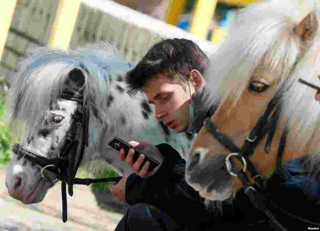 A man uses a mobile phone near his ponies at a park in central Kyiv, Ukraine.