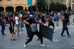 FILE - People throw stones during a protest following the August 4 explosion that killed many and devastated the city, in Beirut, Lebanon, August 11, 2020.