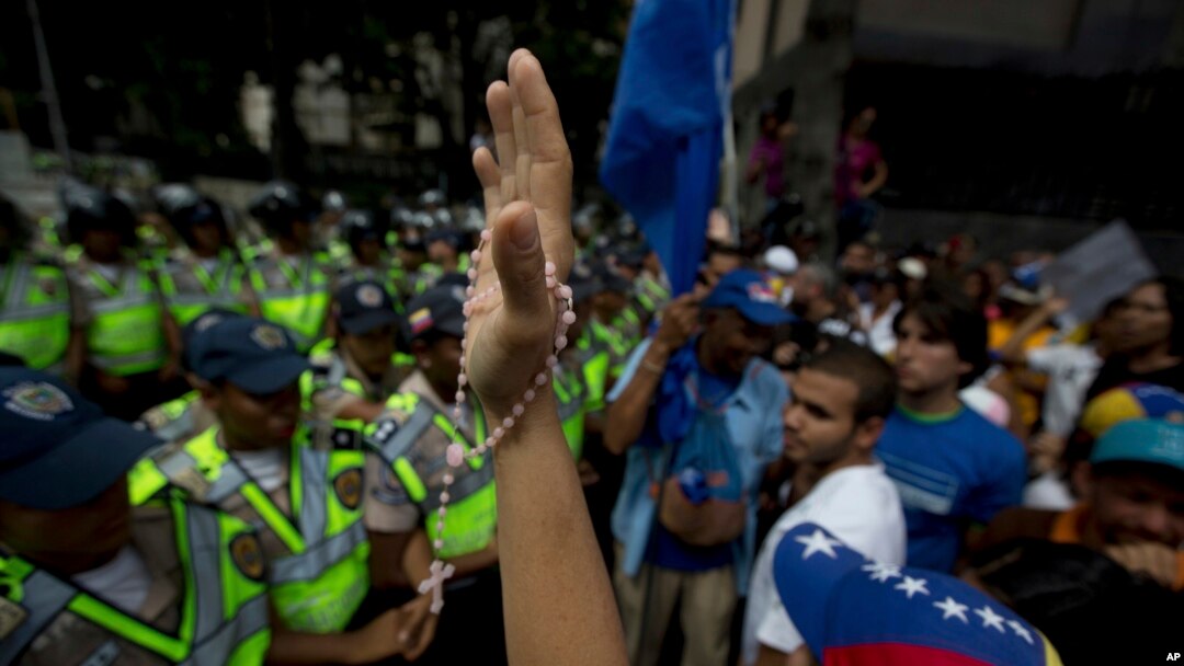 Seorang demonstran mengangkat tangannya yang memegang rosario, dalam protes menentang pemerintah di Caracas, Venezuela (23/1). (AP/Fernando Llano)